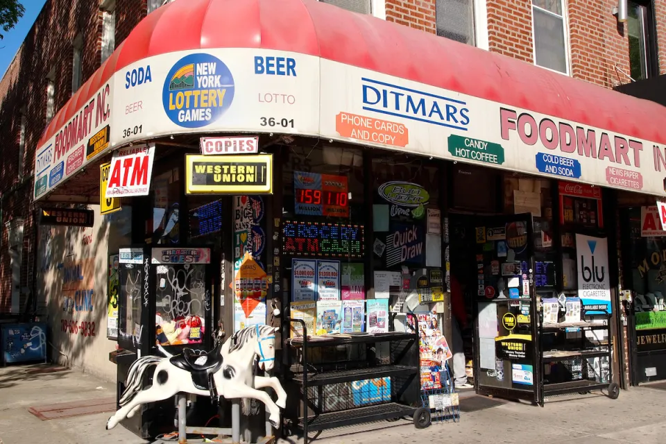Corner convenience store with red awning and children's rocking horse toy out front in brick building in Queens, New York City